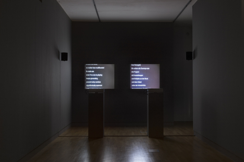 in einem dunklen Raum laufen zwei Videoprojektionen mit Text nebeneinander