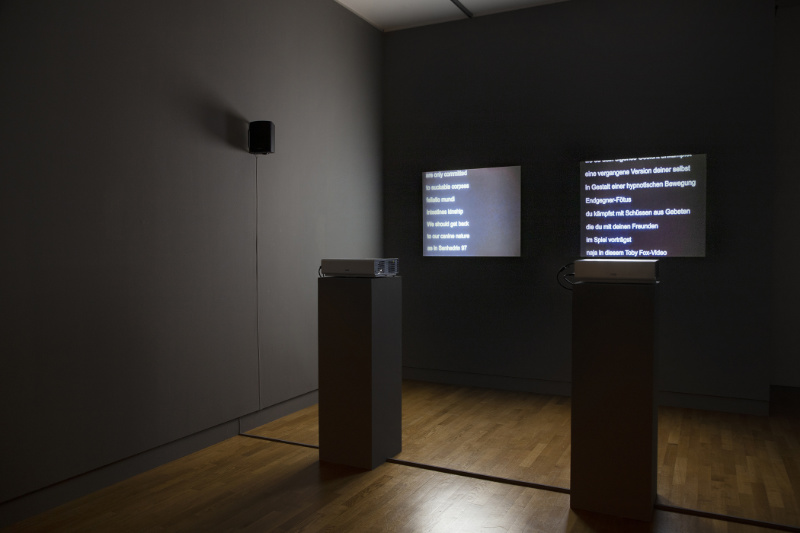 in einem dunklen Raum laufen zwei Videoprojektionen mit Text nebeneinander