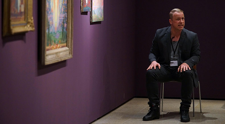 Schauspieler sitzt in einer Ausstellung vor einem Bild
