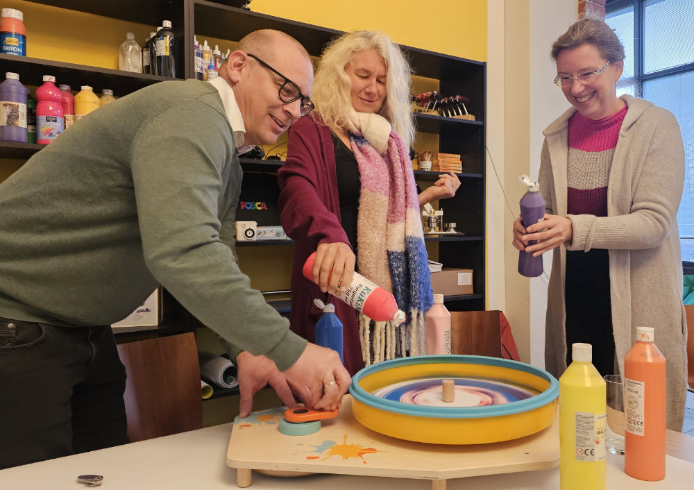 Drei Personen spritzen Farbe in eine Zentrifuge, wodurch zufällige Muster entstehen