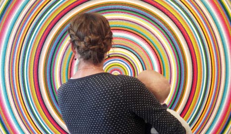 Frau mit Kleinkind auf dem Arm steht mit dem Rücken zum Betrachter vor einem Kunstwerk