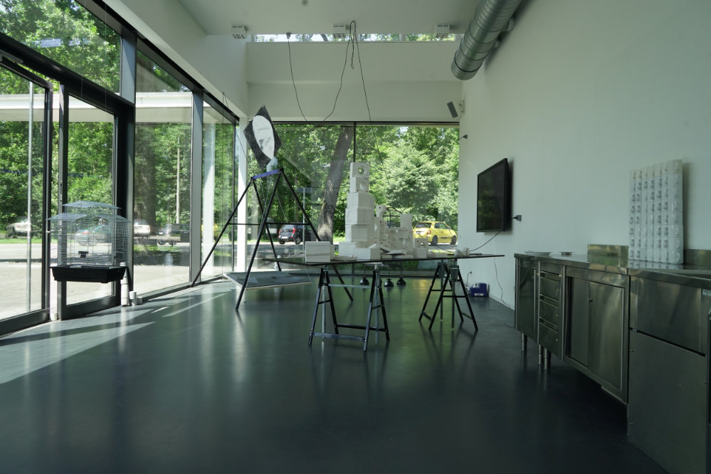 Blick in einen Atelierraum mit einer großen Fensterfläche, auf einem Tisch stehen weiße Objekte