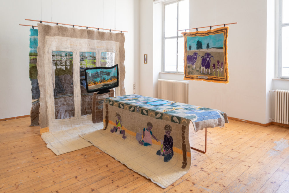 große bestickte Leinwände liegen und hängen im Raum