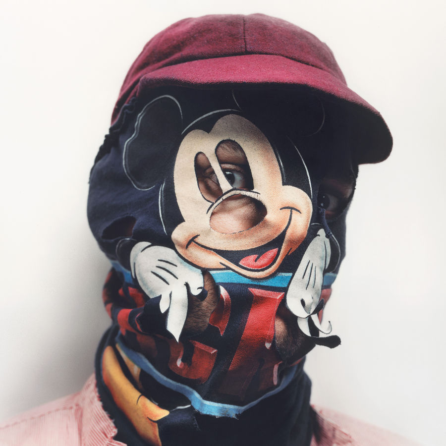 der Kopf einer Person mit einer Haube, die das Gesicht verdeckt. Nur die Augen schauen heraus. Auf der Haube ist eine Mickey Maus gedruckt.