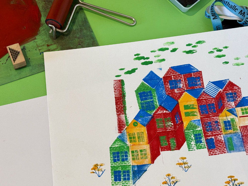 eine bunte Druckgrafik, die eine Stadt darstellt, daneben liegen verschiedene Druckwerkzeuge