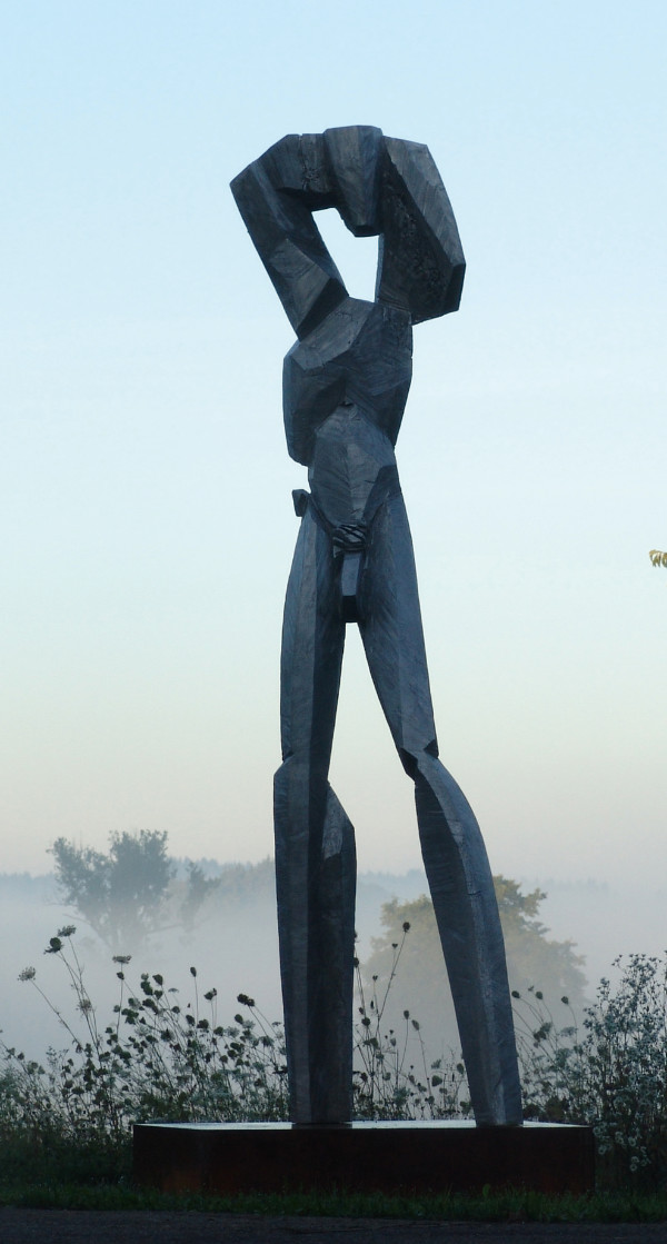 Überlebensgroßes schwarze Aluminiumskulptur eines nackten Mannes auf einer Lichtungg