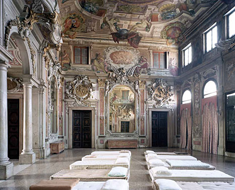 Saal in einem Schloss, auf dem Boden liegen einfache Betten in zwei Reihen