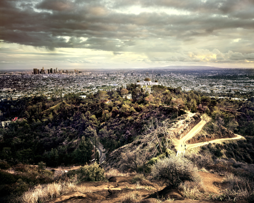 Blick von einer Anhöhe über eine Stadt mit Hochhäusern und Bergen im Hintergrund